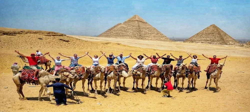 A group of tourists riding camels in front of Giza Pyramids during their Egypt Shore Excursions from the port.