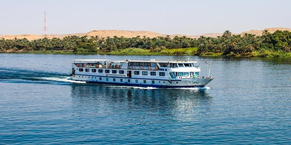 A luxury cruise ship sailing on the water during Nile River Cruises, featuring scenic views of the Nile banks and palm trees.
